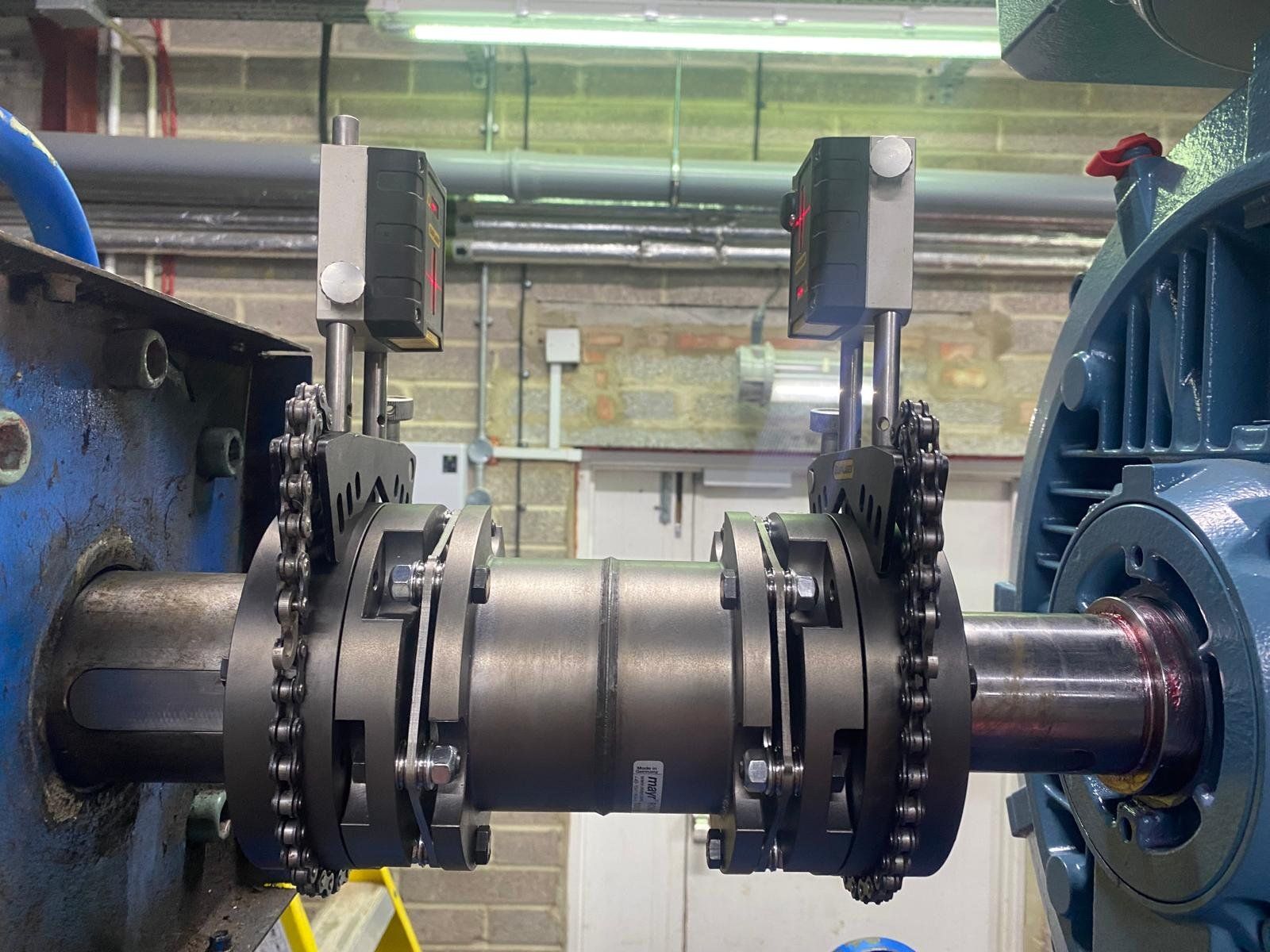 Industrial machinery with chains and a large metal shaft in a workshop environment.