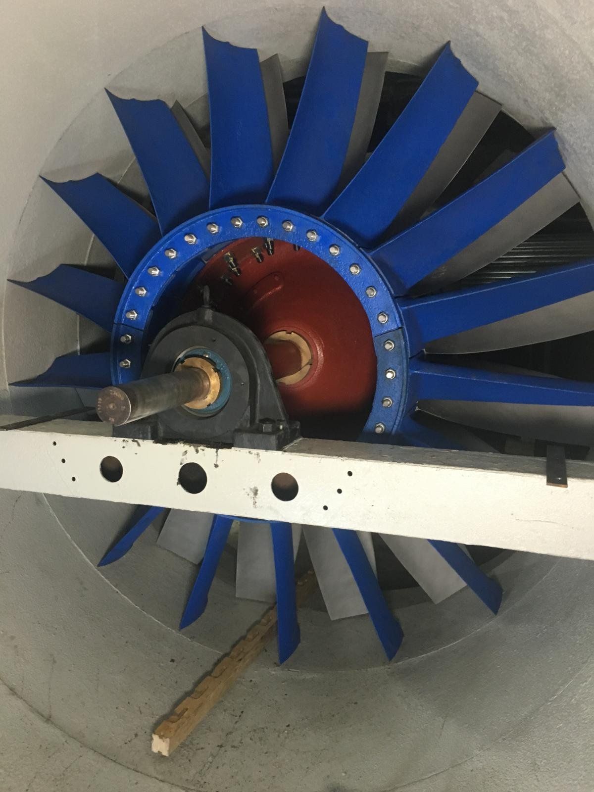 Close-up of a large industrial turbine or fan with blue blades inside a concrete shaft.