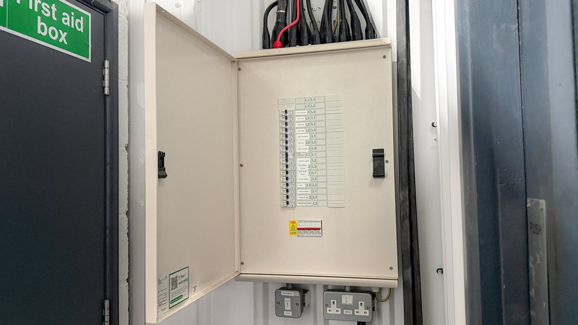 Electricity fuse box with various circuit labels and switches, mounted on a wall in a utility or electrical room.